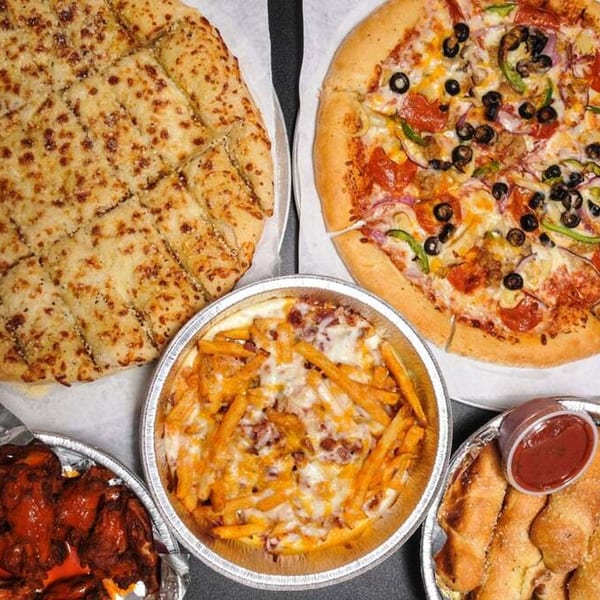 A Gumby's Pizza spread with a supreme pizza, cheesy bread, loaded fries, wings, and breadsticks.
