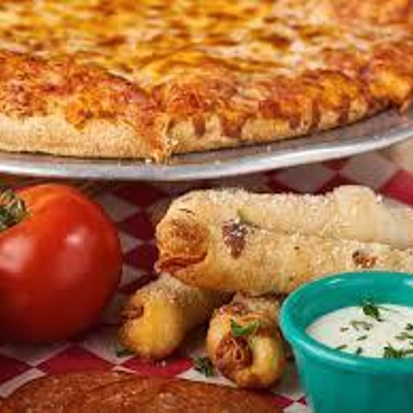 A Gumby's Pizza with a side of breadsticks, a tomato, and a dipping sauce.