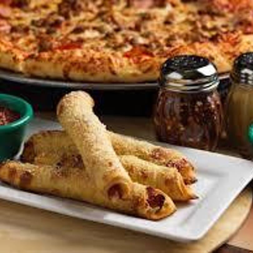 A Gumby's Pizza pepperoni pizza with three pepperoni rolls and shakers of spices.