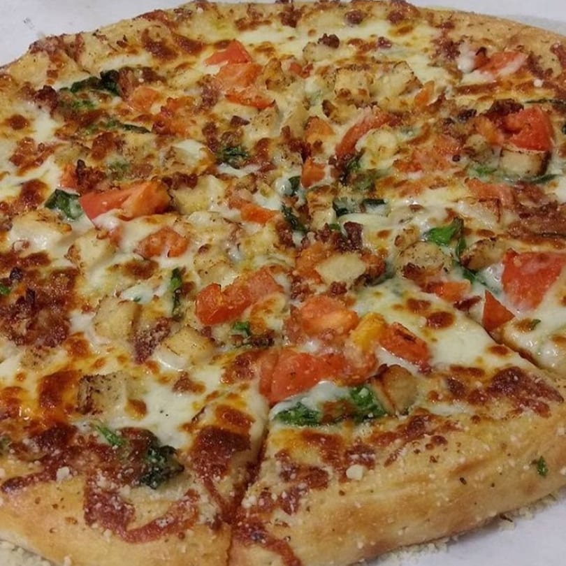 A close-up of a Gumby's Pizza with chicken, bacon, tomatoes, and spinach.