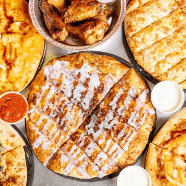 A spread of Gumby's Pizza items, including a cinnamon dessert pizza, garlic knots, and chicken wings.