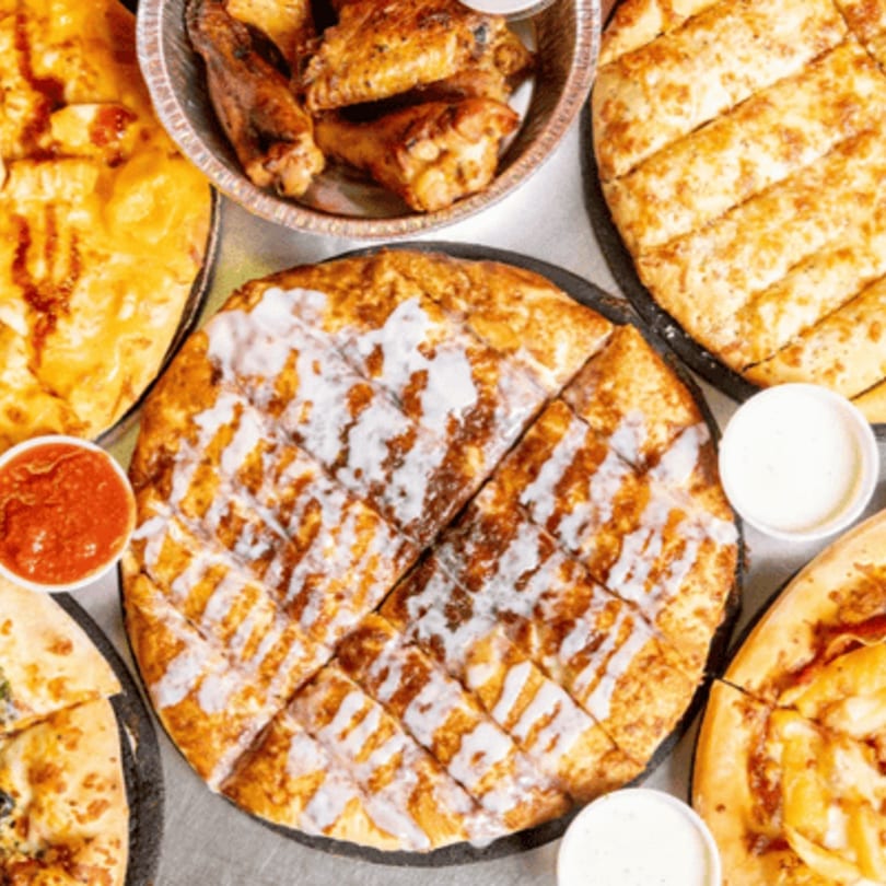 A spread of Gumby's Pizza items, including a cinnamon dessert pizza, garlic knots, and chicken wings.