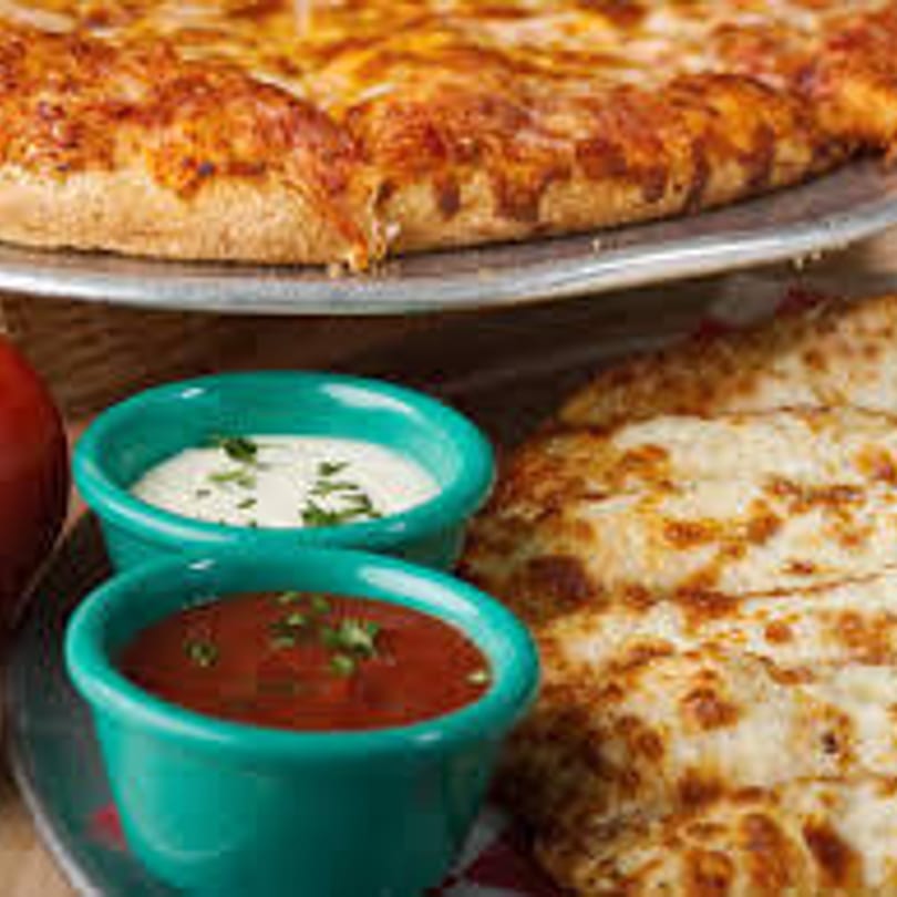 Gumby's Pizza with cheese breadsticks and dipping sauces in teal bowls.