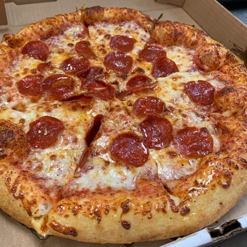 A whole Gumby's pepperoni pizza with melted cheese and a golden crust in a cardboard box.