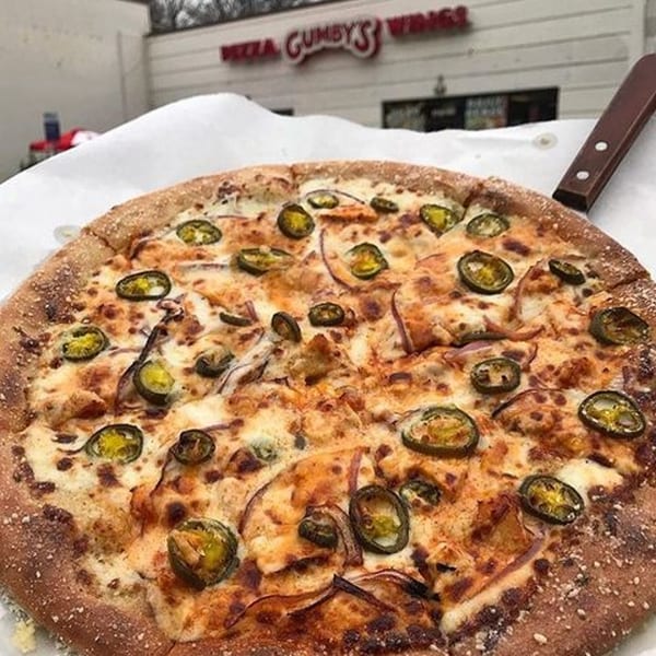 A Gumby's Pizza with jalapeños and onions, with the restaurant sign in the background.