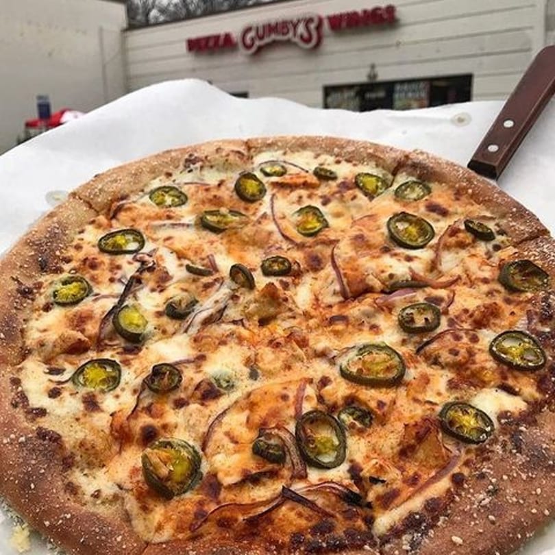 A Gumby's Pizza with jalapeños and onions, with the restaurant sign in the background.