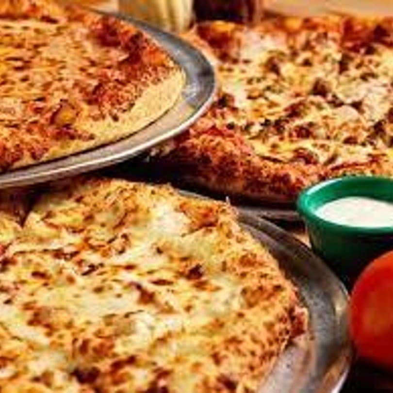 Three Gumby's pizzas on metal trays, with a side of ranch dressing and a tomato.